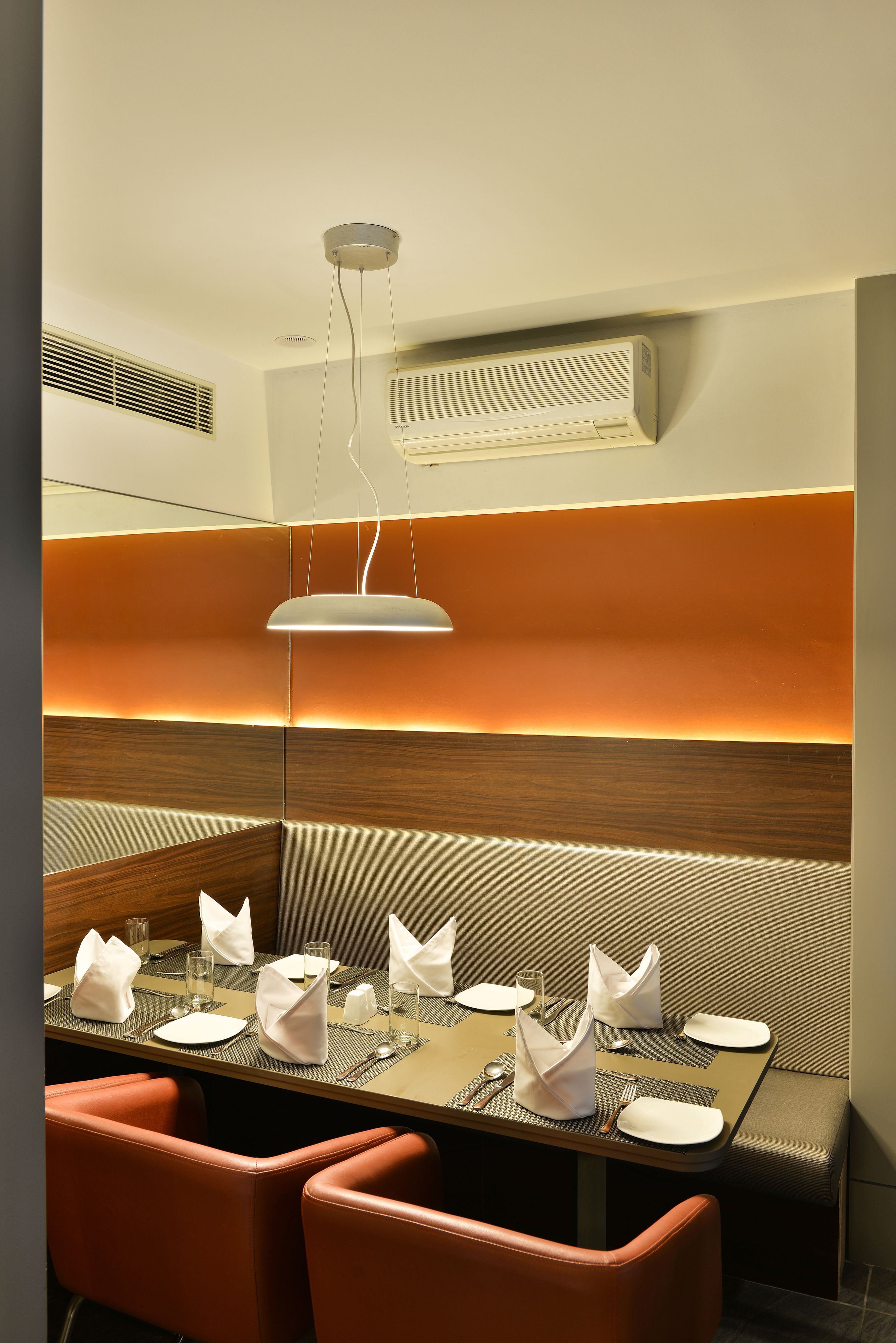 A dining area with a table set for four, including plates, glasses, and cutlery. There are orange upholstered chairs and a modern pendant light above the table.