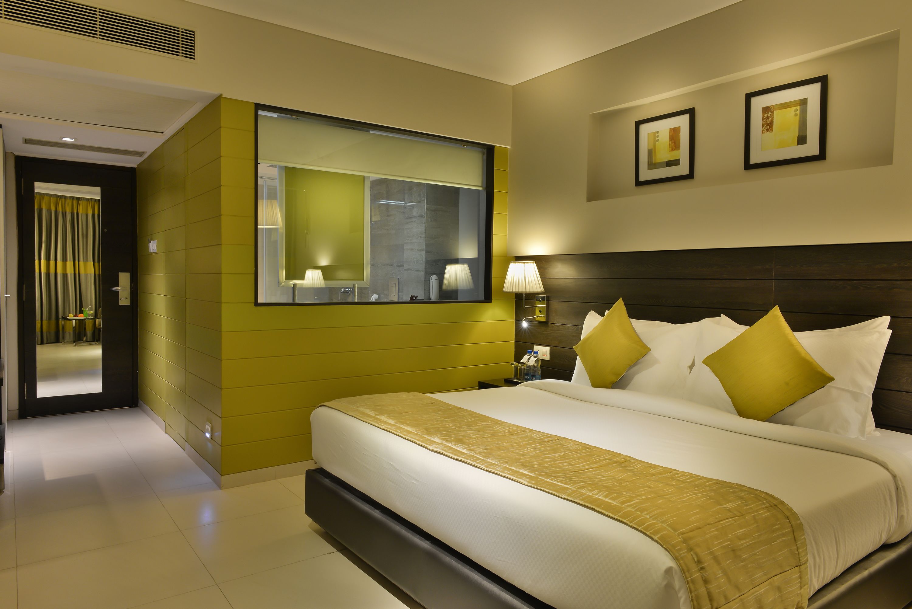 Une chambre d’hôtel moderne avec un grand lit, une table de chevet, un miroir et une lampe fixée au mur.