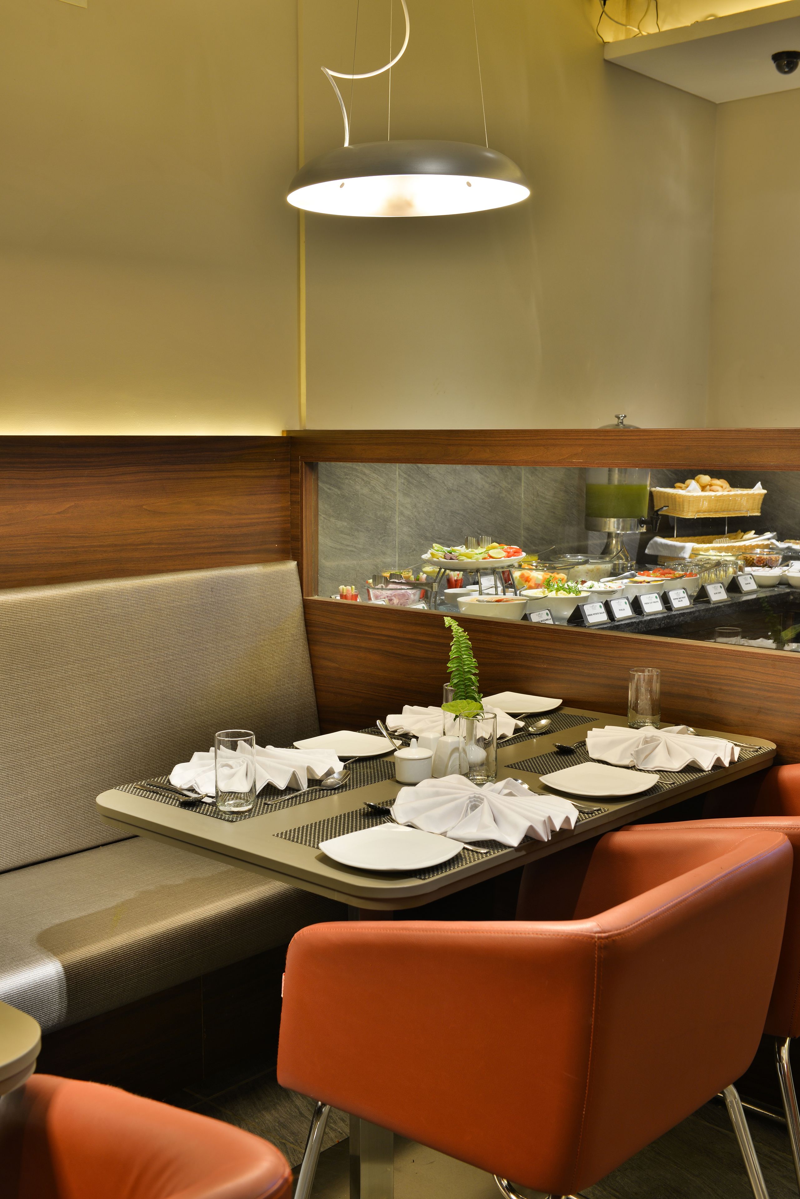 A restaurant with a buffet setup, a seating area with a cushioned bench, and a modern pendant light.