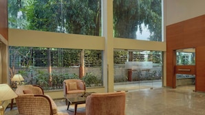 Eine großzügige Lobby mit hohen Decken, großen Fenstern und Blick auf üppiges Grün. Bequeme Sitzbereiche mit Sofas und Sesseln vorhanden.