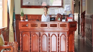 A reception desk with a wooden finish, a potted plant, and a framed picture on the wall. - Rotha Guesthouse (Siem Reap)