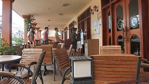 A covered outdoor seating area with wooden benches and tables, a covered walkway, and a building with wooden doors and windows. - Rotha Guesthouse (Siem Reap)
