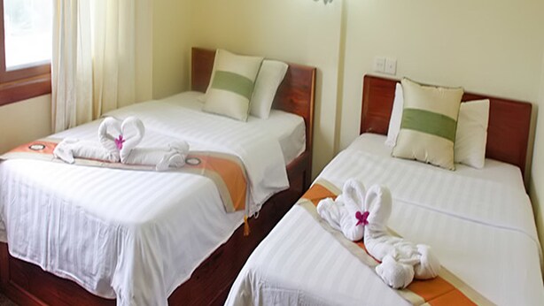 Two adjacent hotel rooms with wooden headboards, white bedding, and towels arranged on the beds. - Rotha Guesthouse (Siem Reap)