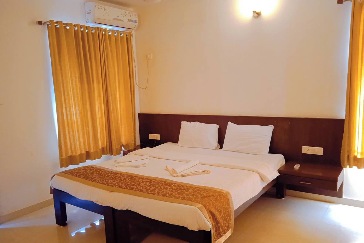 A hotel room with a bed, a nightstand, a wall-mounted air conditioner, and curtains.