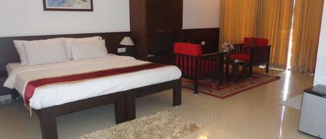 A hotel room with a bed, a desk, a chair, a lamp, a picture on the wall, and a window with curtains.