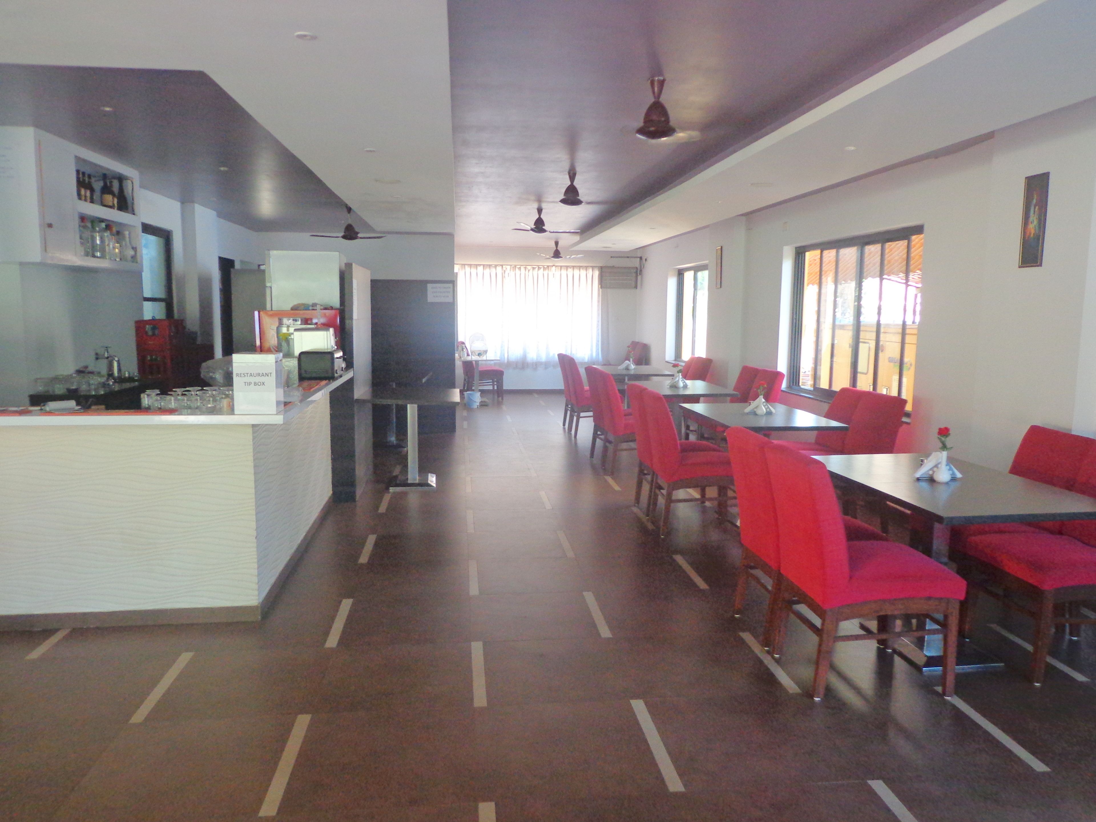 A restaurant with a long counter, red chairs, and a dining area with tables.