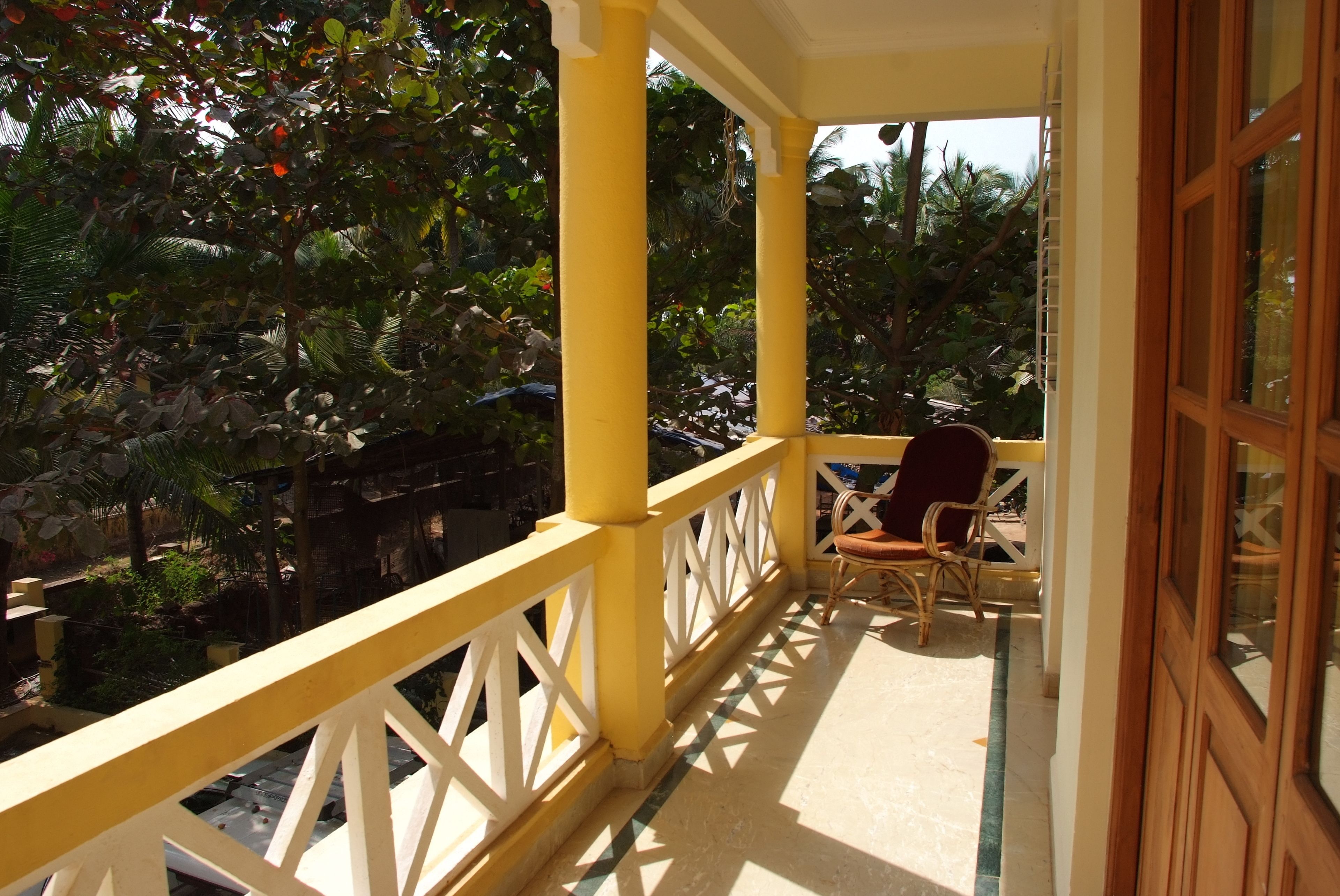 A balcony with yellow railings, a wicker chair, and a view of lush greenery.