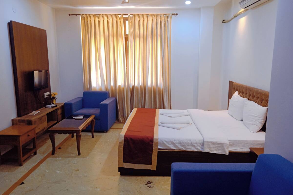 A hotel room with a bed, a desk, a chair, a television, and a window with curtains.