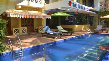Una piscina con sillas de descanso y sombrillas, un bar junto a la piscina y un edificio con un letrero que dice "The Tubki Resort".