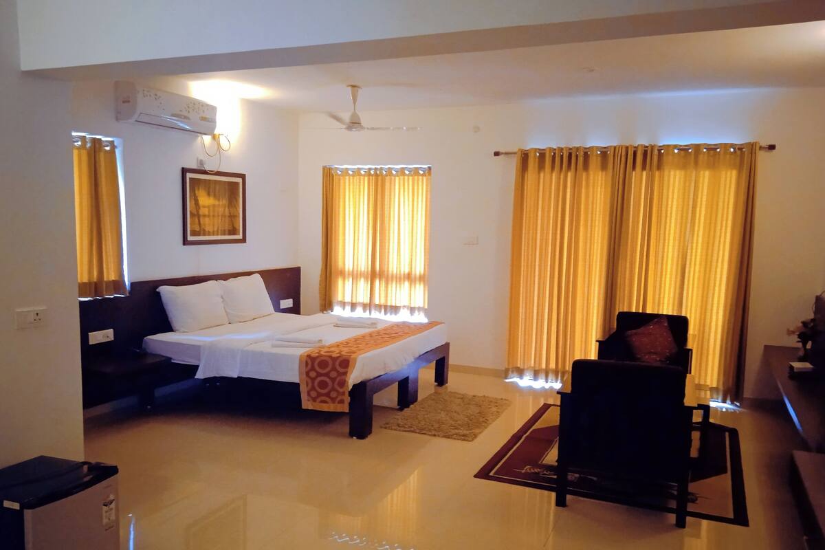 A hotel room with a bed, a sofa, a chair, a small table, and a window with curtains.