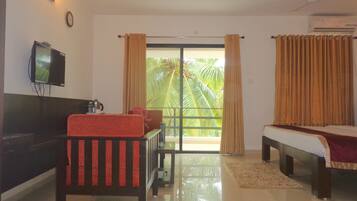 A hotel room with a bed, a sofa, a TV, a balcony with curtains, and a ceiling fan.