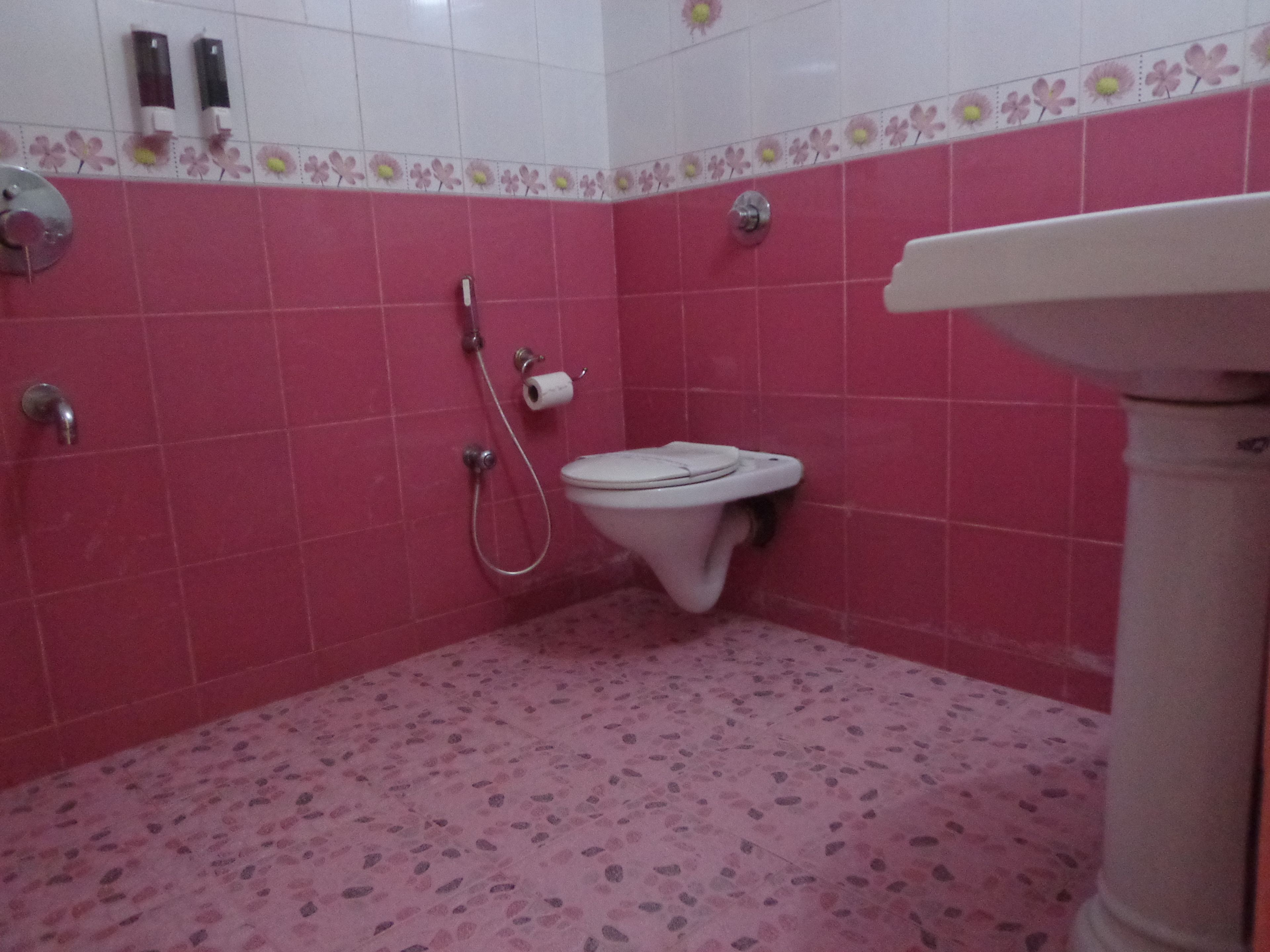 A bathroom with pink tiles, a toilet, a shower, and a sink.