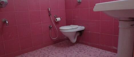 A bathroom with pink tiles, a toilet, a shower, and a sink.