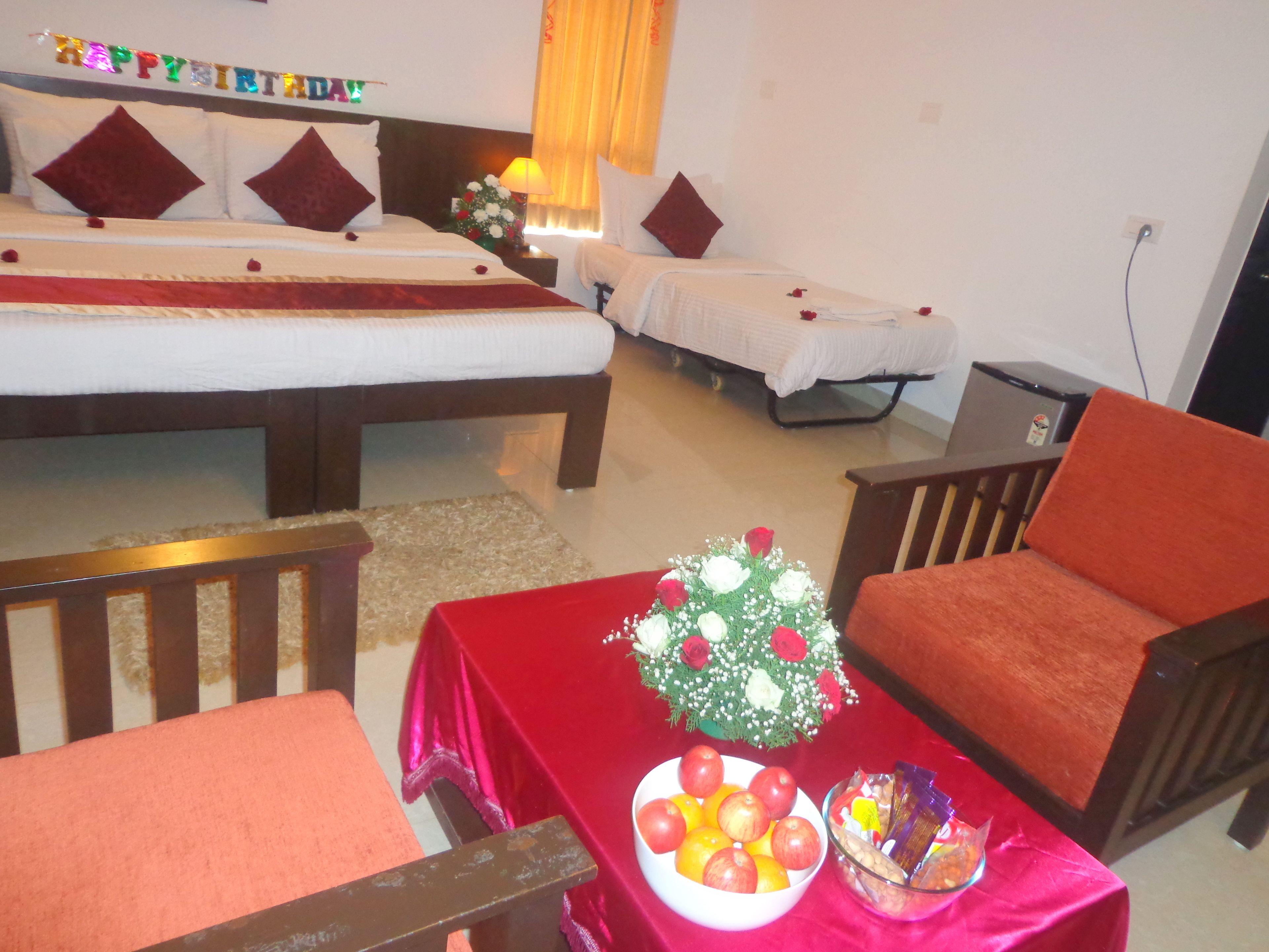 A hotel room with two beds, a dining table with fruit and snacks, and a red chair.