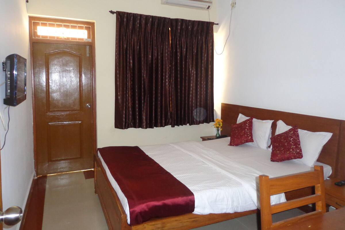 A neatly made bed with a wooden headboard, a dark curtain, and a wall-mounted air conditioner.