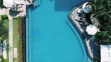 An aerial view of a swimming pool with lounge chairs and umbrellas, surrounded by greenery.