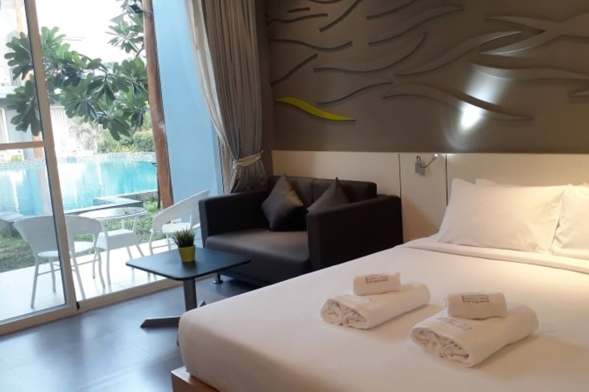 A hotel room with a bed, a sofa, a small table, and a view of a pool.