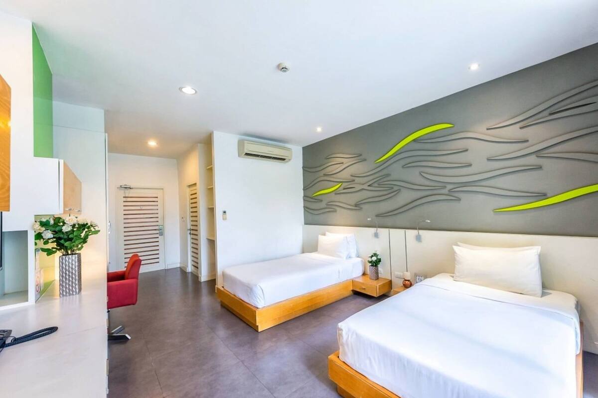 A modern hotel room with two beds, a red chair, a vase with flowers, and a wall with abstract art.