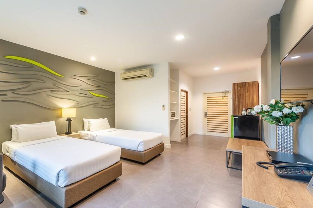 A hotel room with two beds, a desk with a phone, a chair, a wall-mounted air conditioner, and a door leading to another room.