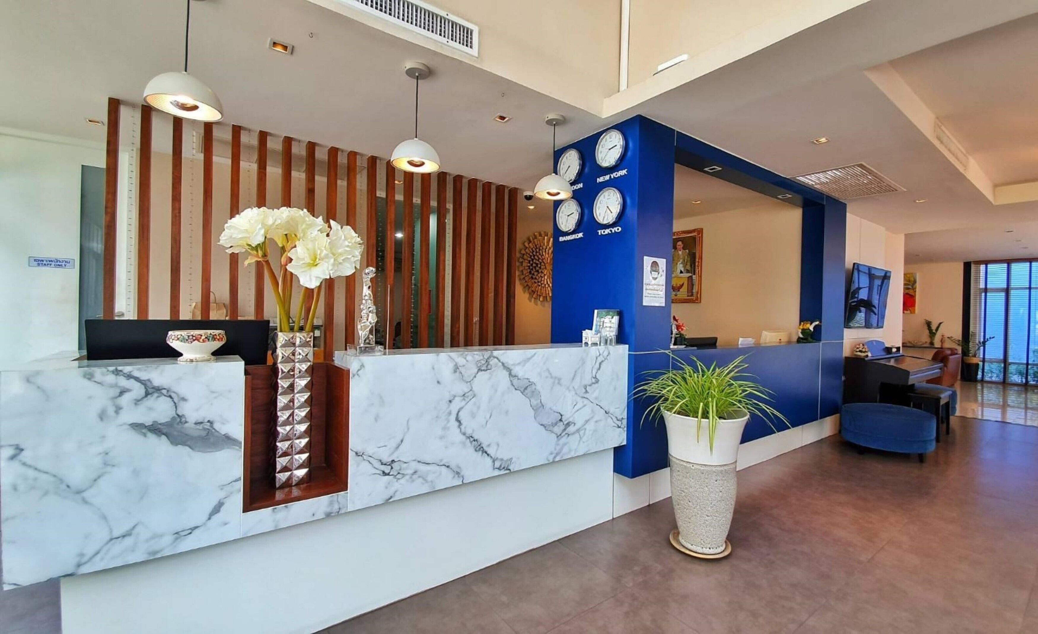A modern reception area with a marble counter, wooden accents, and a clock displaying time in various cities.