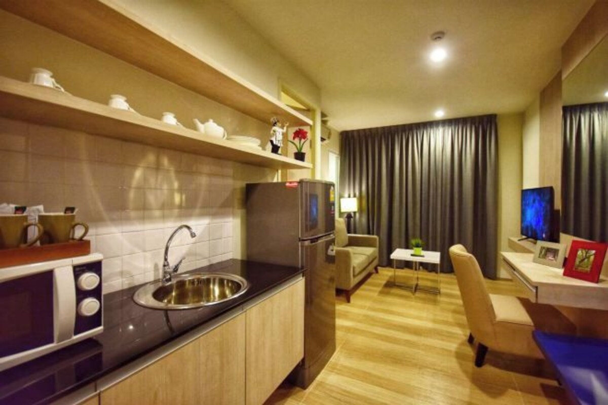 Een compacte hotelkamer met kitchenette, een eethoek met een klein tafeltje en stoelen, een televisie en een groot raam met gordijnen.