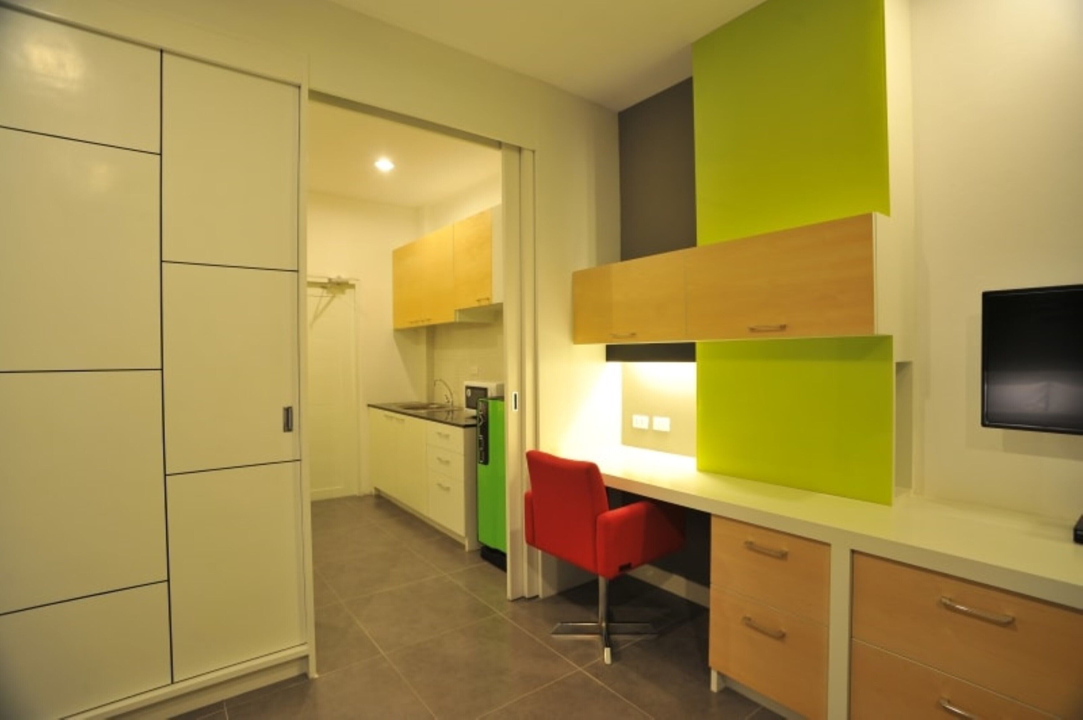 Een moderne keuken met witte kasten, een groen apparaat en een rode stoel.