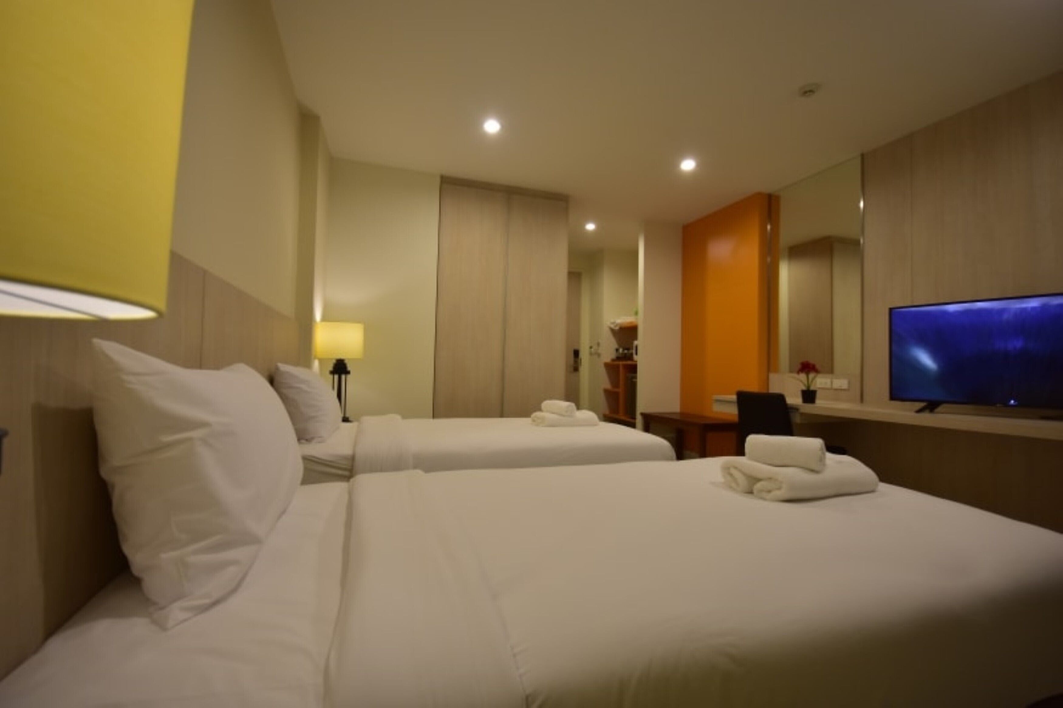 A hotel room with two beds, a television, a desk, and a mirror.