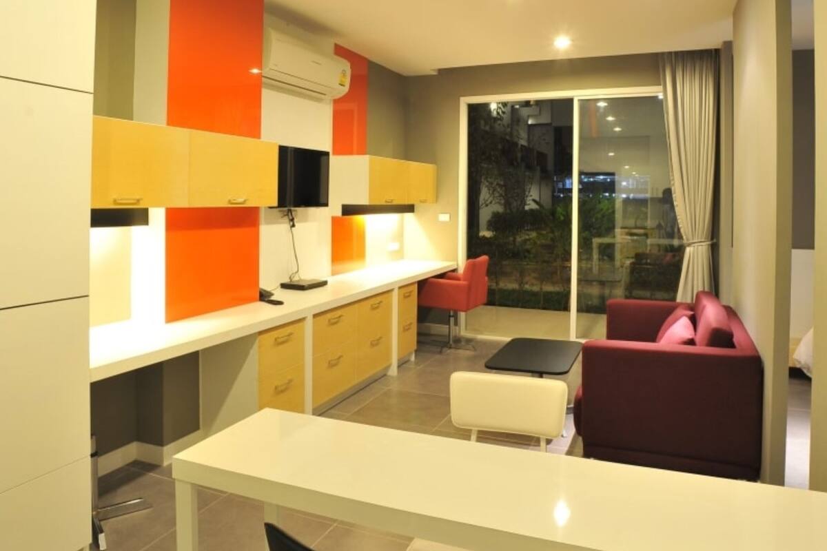 A modern kitchen with a white countertop, yellow and orange cabinets, and a red chair.