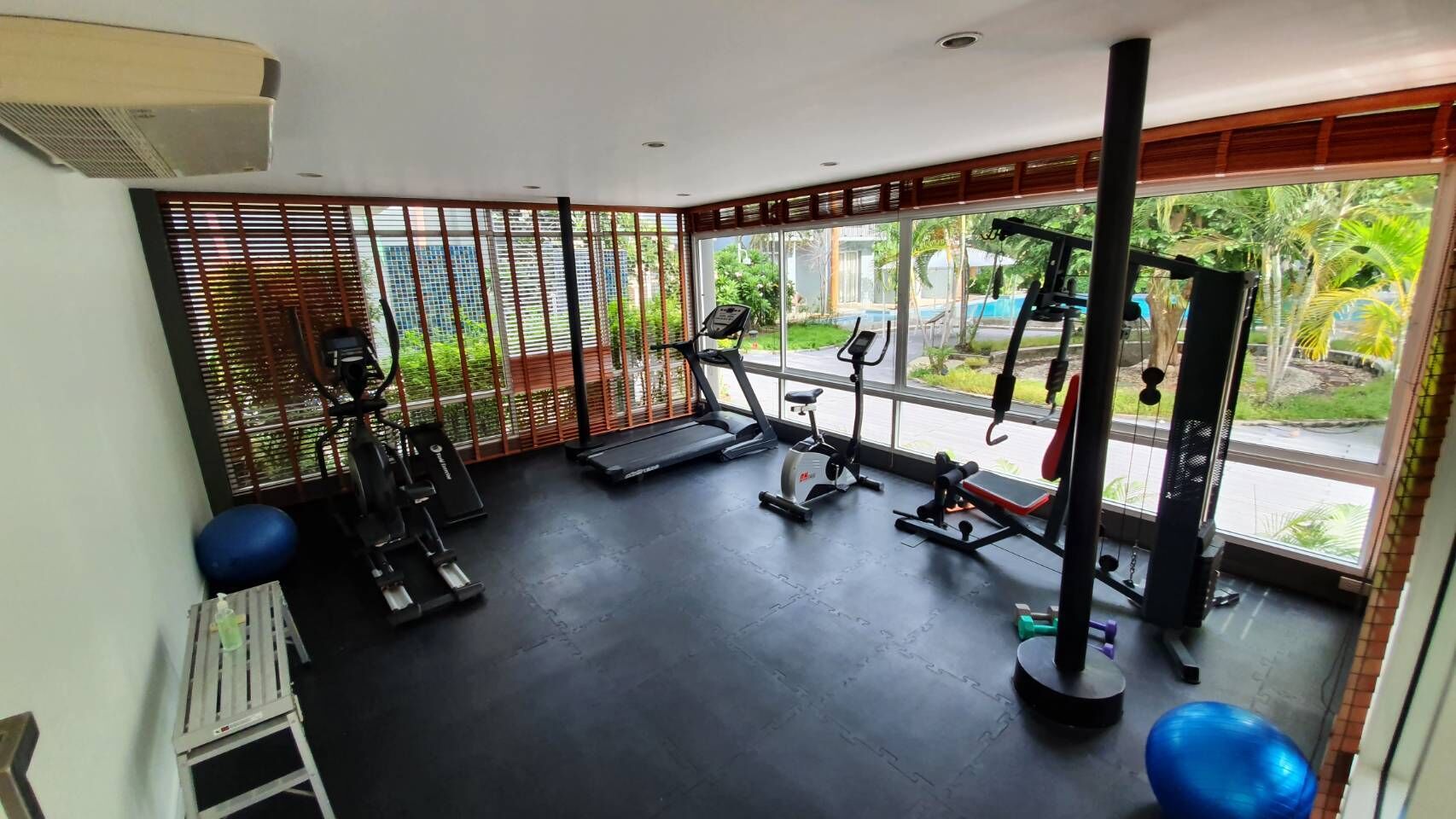 Een sportschool met fitnessapparatuur, een loopband en een raam met uitzicht op groen.