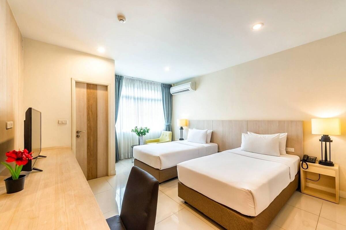 A hotel room with two beds, a desk, a chair, a TV, and a window with curtains.