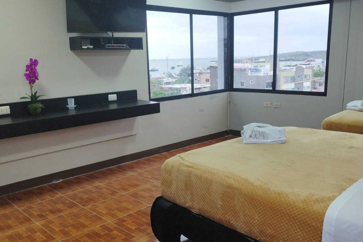 Habitación de hotel con una cama grande, un televisor de pantalla plana en la pared, una ventana con vistas a la ciudad y suelo de baldosas.
