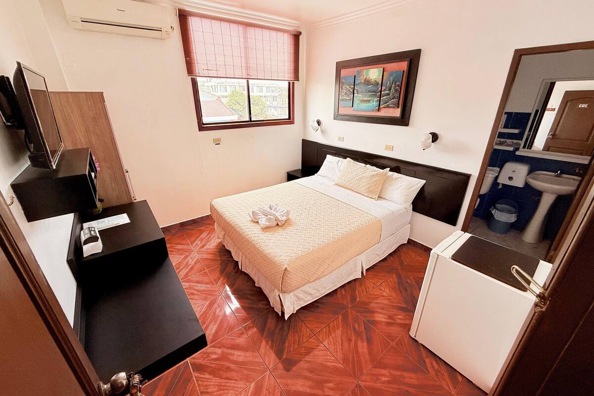Una habitación de hotel con cama, escritorio, espejo, ventana y baño.