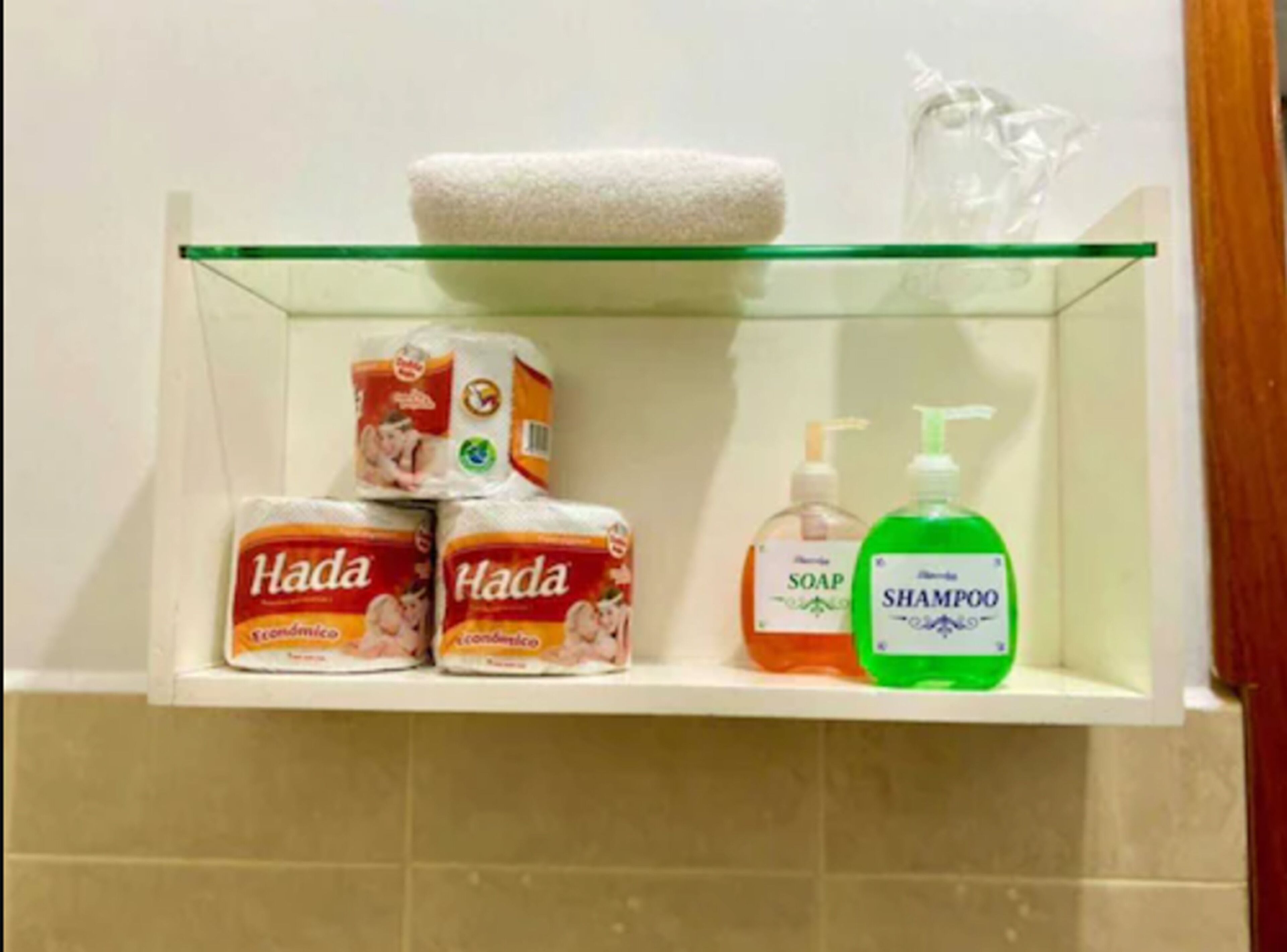 A bathroom shelf with toilet paper, soap, and shampoo.