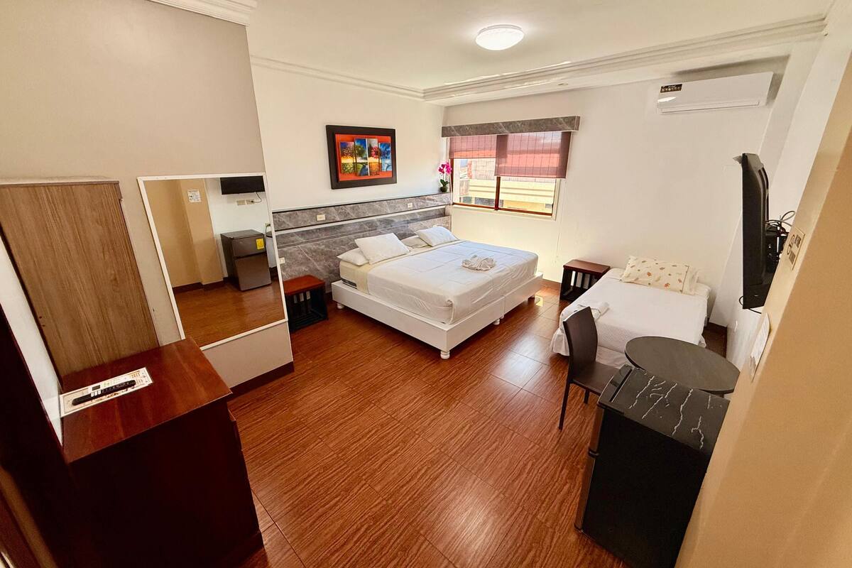 Habitación de hotel pequeña con una cama, un escritorio, una silla, televisión y ventana con vistas.