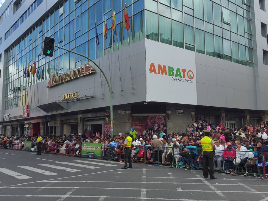 Un hotel con fachada de vidrio moderna, una señal visible que dice 'AMBATO' y un cartel que indica 'HOTEL'.