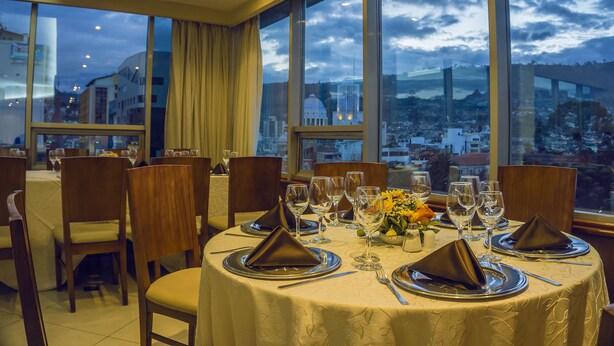 A dining area with tables set for four, large windows, and a view of the cityscape. - Hotel Emperador (Ambato)