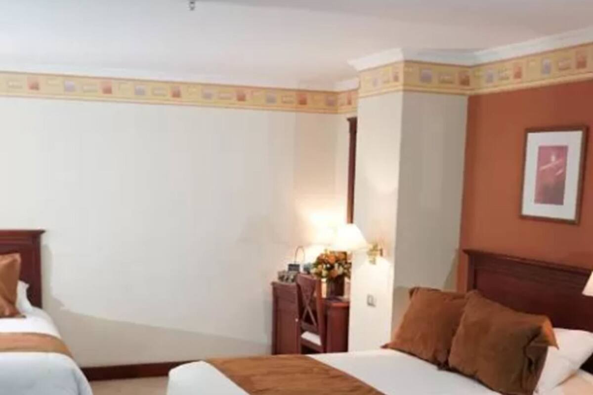 A hotel room with two beds, a nightstand, and a lamp.