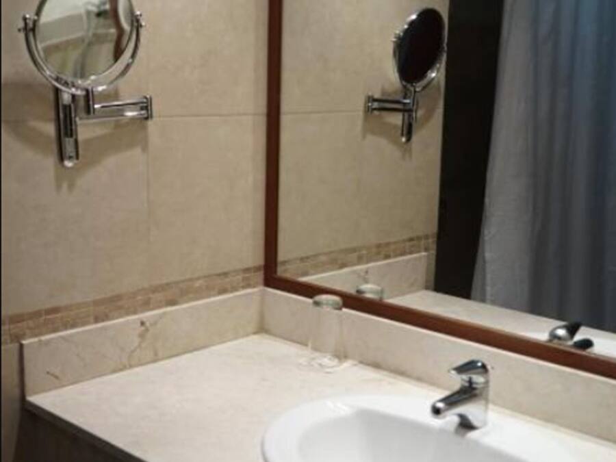 Un baño con un lavabo blanco, dos espejos redondos y un perchero para toallas.