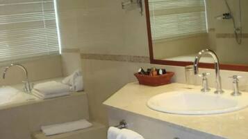 A modern bathroom with a large sink, a bathtub, and a shower. There is a mirror above the sink and a window with blinds.