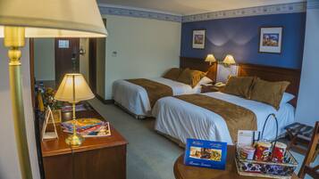Ein Hotelzimmer mit zwei Betten, einem Schreibtisch mit Lampe, einem Sessel, einem kleinen Tisch mit Snacks und einer Minibar.