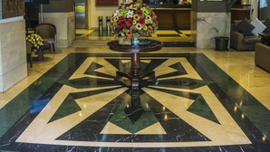 A hotel lobby with a reception desk, a large floral centerpiece, and a patterned floor. - Hotel Emperador (Ambato)