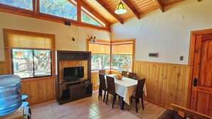 Un salon spacieux avec un plafond en bois, de grandes fenêtres, une cheminée, une table à manger avec des chaises et un canapé.