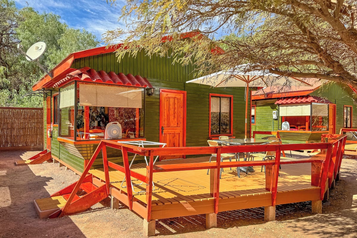 A rustic cabin with a wooden deck, a dining area, and a covered seating area.