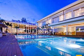 A modern hotel with a large outdoor swimming pool, sun loungers, and a well-lit reception area. - Chi Samui Resort (Koh Samui)