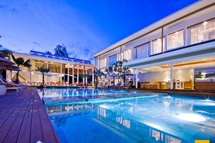 A modern hotel with a large outdoor swimming pool, sun loungers, and a well-lit reception area.