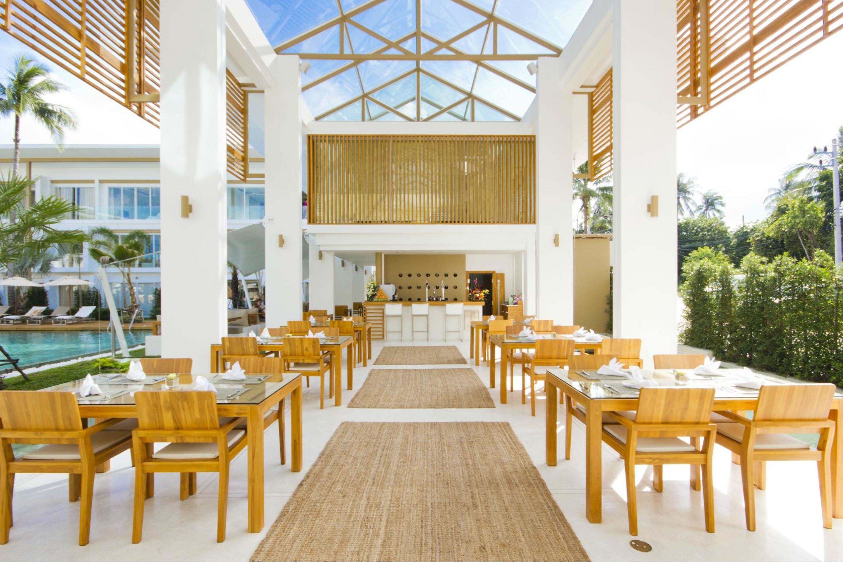 Un comedor espacioso con mesas y sillas de madera, una barra central y vistas a la piscina.