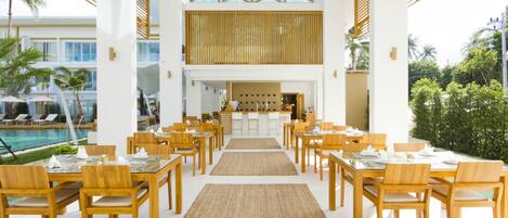 Un comedor espacioso con mesas y sillas de madera, una barra central y vistas a la piscina.