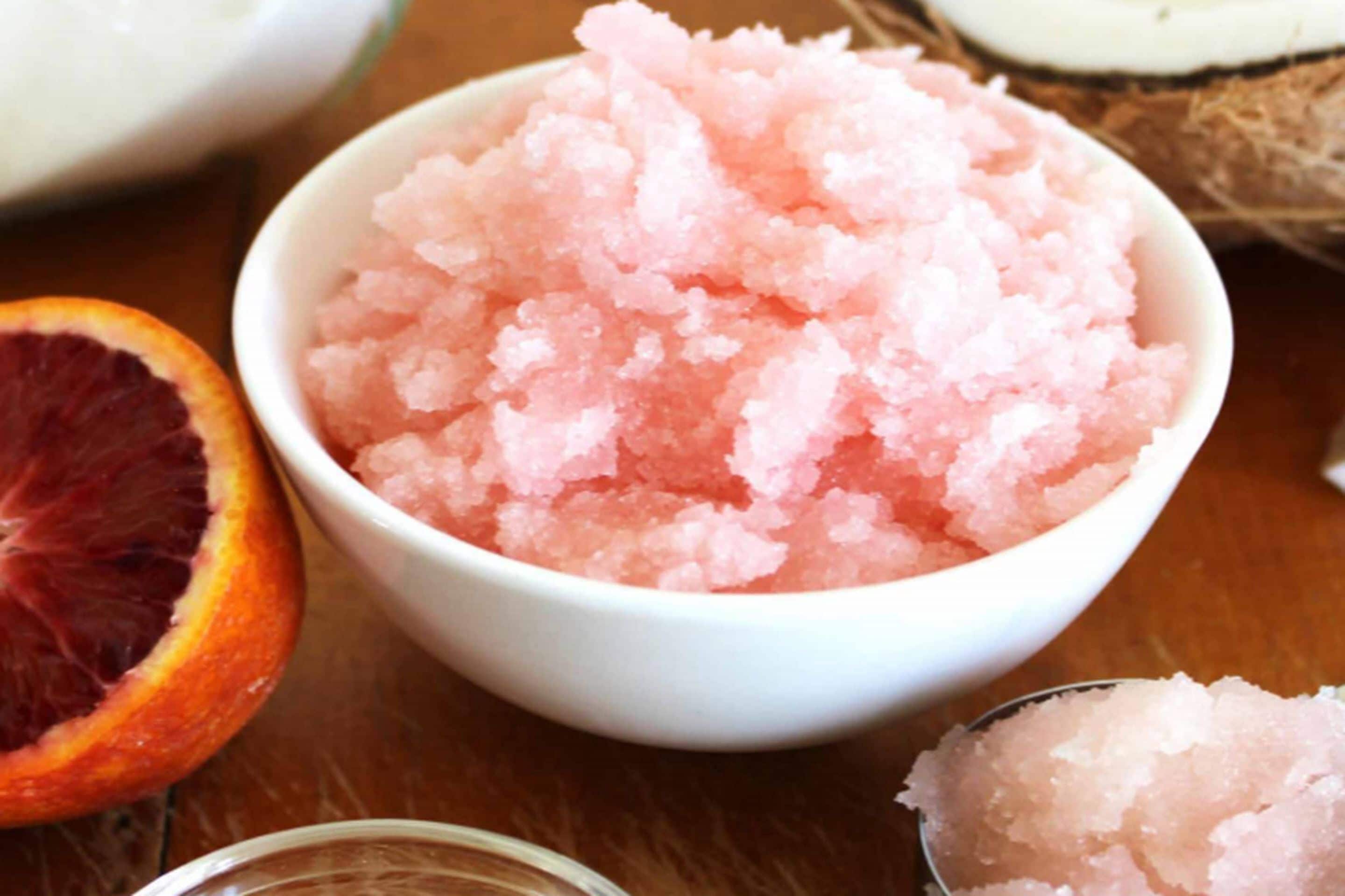 A bowl of pink bath salts with a half-cut orange and a coconut shell in the background.