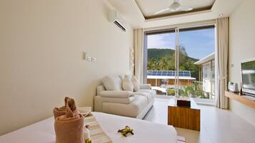 A modern hotel room with a large bed, a sofa, a TV, and a view of a mountain and solar panels.