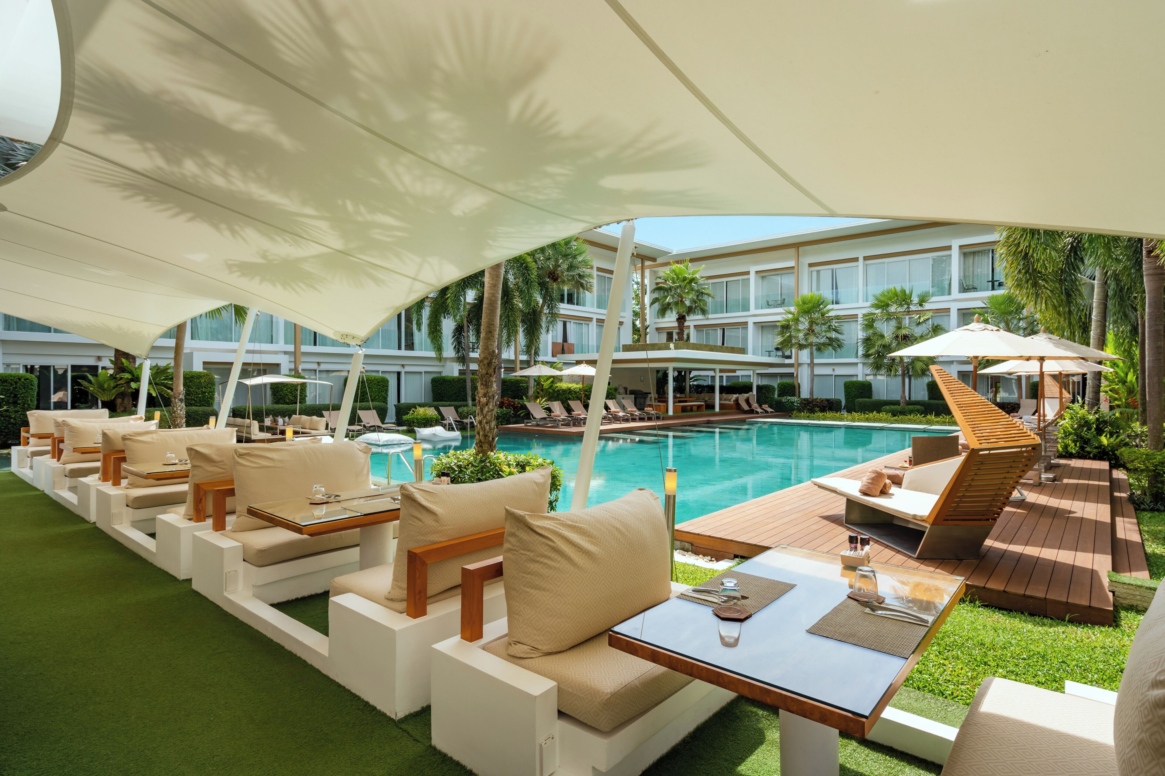 A poolside area with lounge chairs and tables, a pool, and a building in the background.